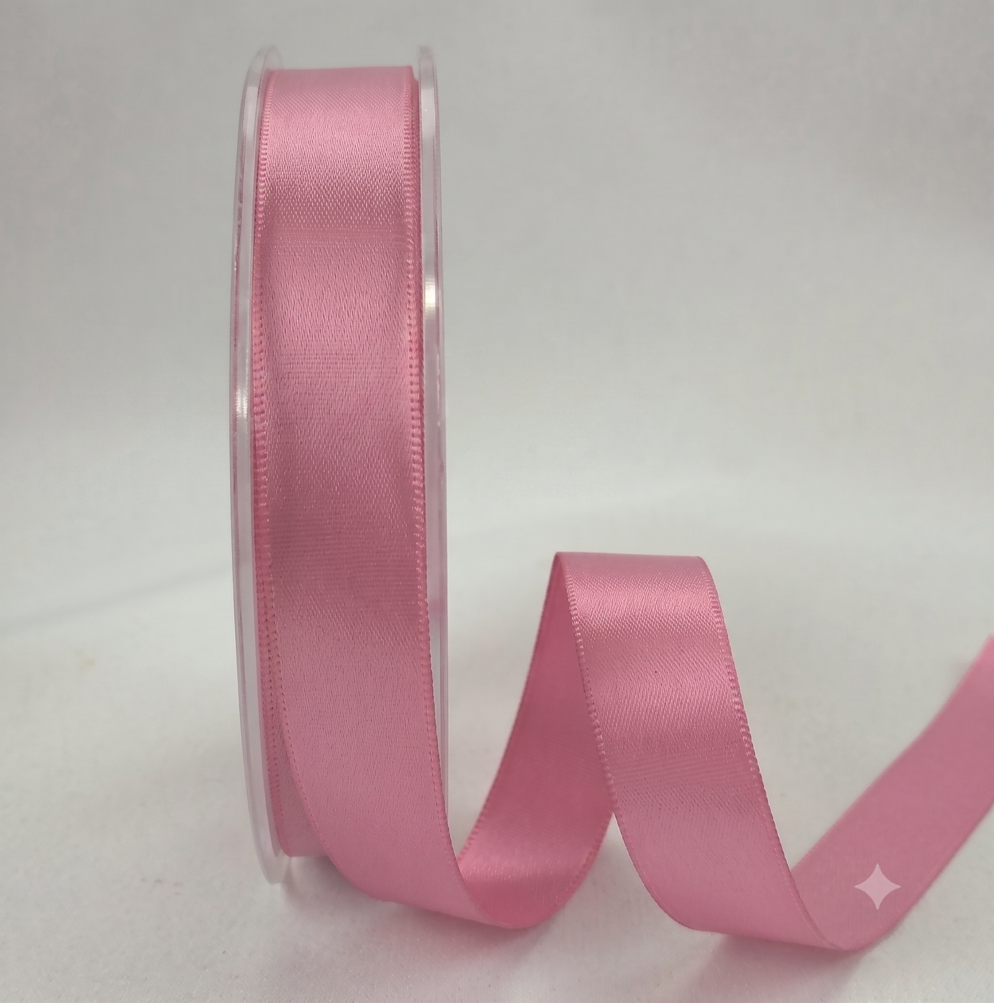 A roll of pink satin ribbon with a length unspooled in a curved loop, set against a plain light gray background.