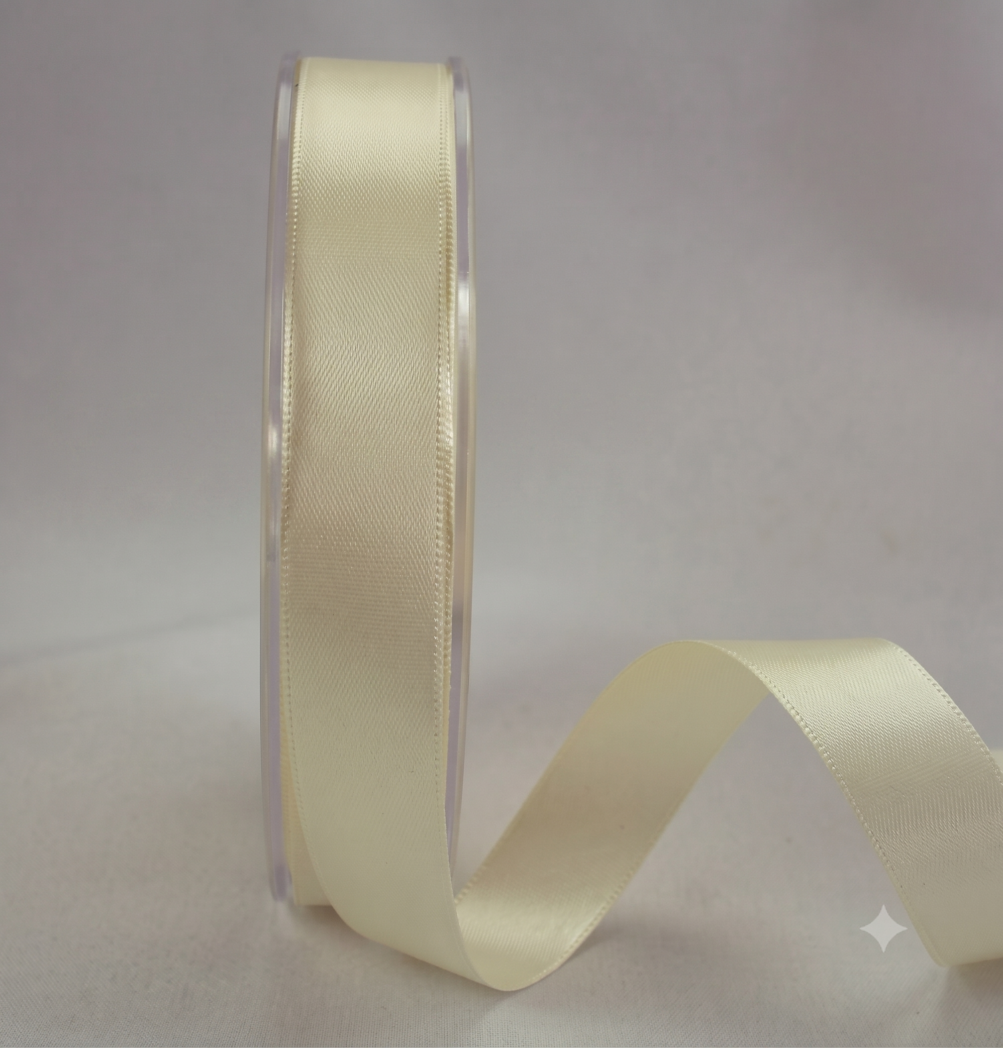 A roll of cream-colored satin ribbon on a clear plastic spool, with the ribbon draped out to the right against a neutral light gray background.