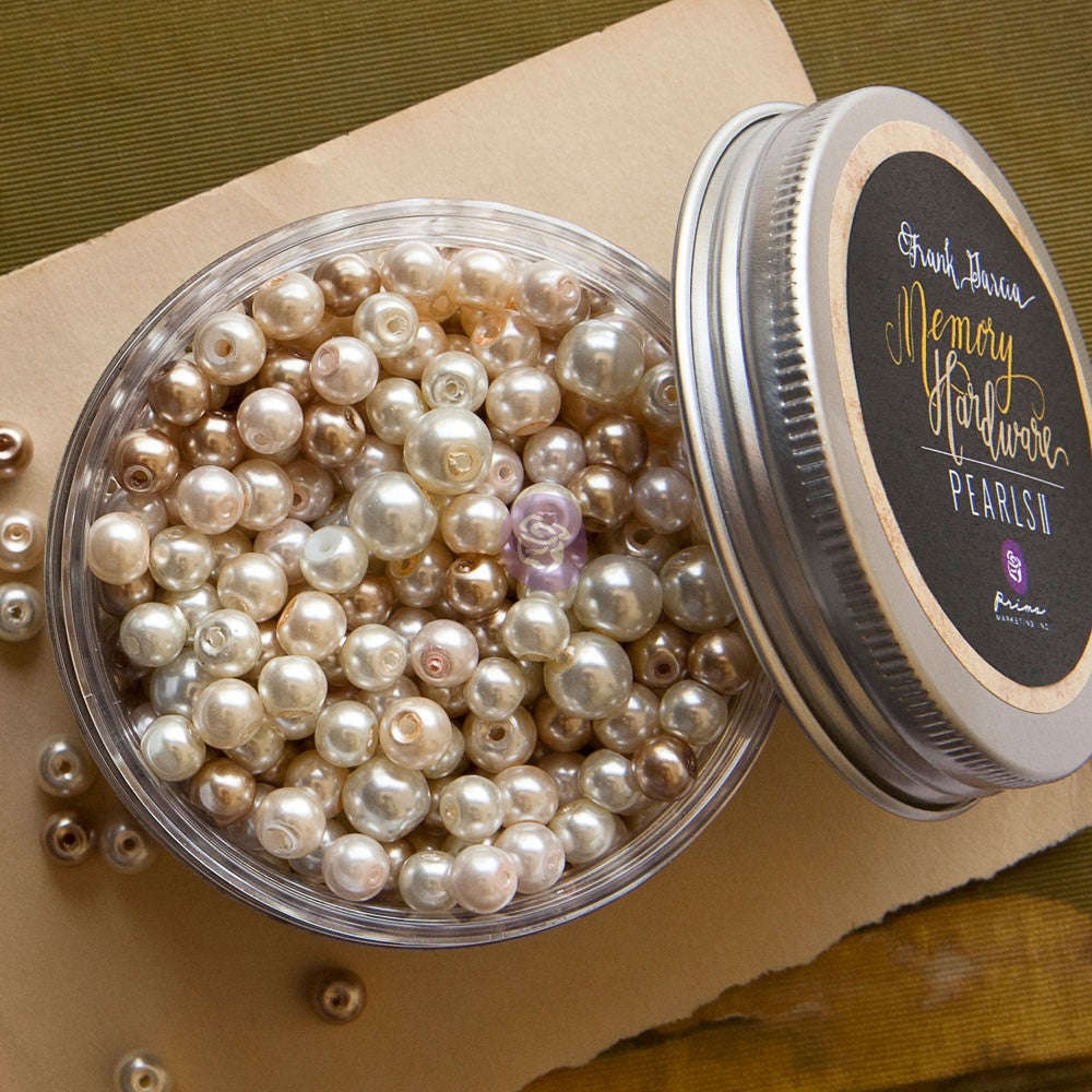 An open round clear jar filled with pearl-like beads in champagne, cream, and pale gold tones, shown beside a silver lid with a black label reading 'Grand Thera Memory Pearls'.
