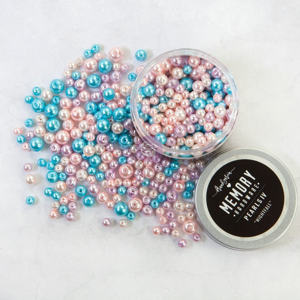 A collection of iridescent freshwater pearls in pastel pink, blue, and lavender, with one open jar showing the pearls inside, a pile spilled out, and a silver tin lid labeled 'Memory Pearls'.