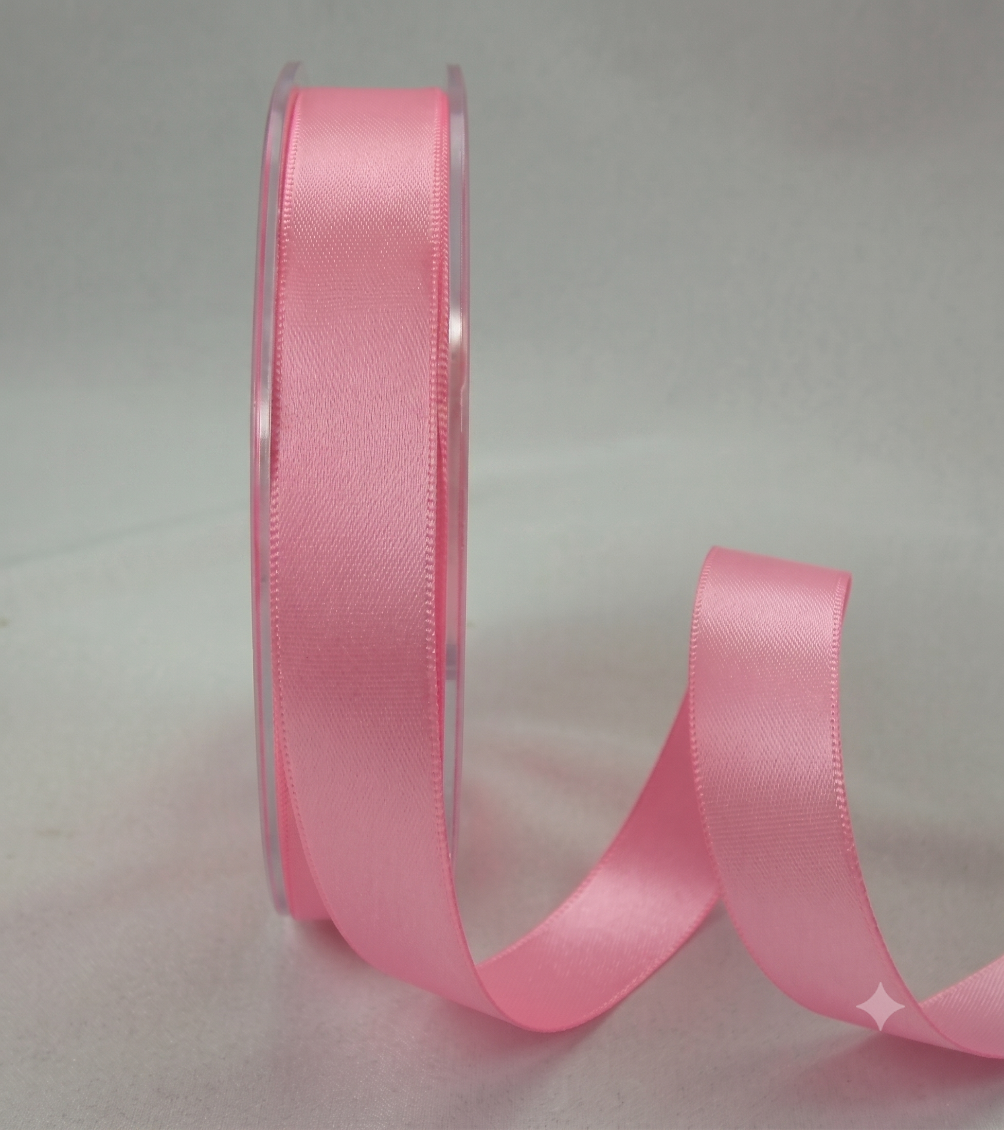A roll of light pink satin ribbon with a length of the ribbon unspooled, set against a neutral light gray background.