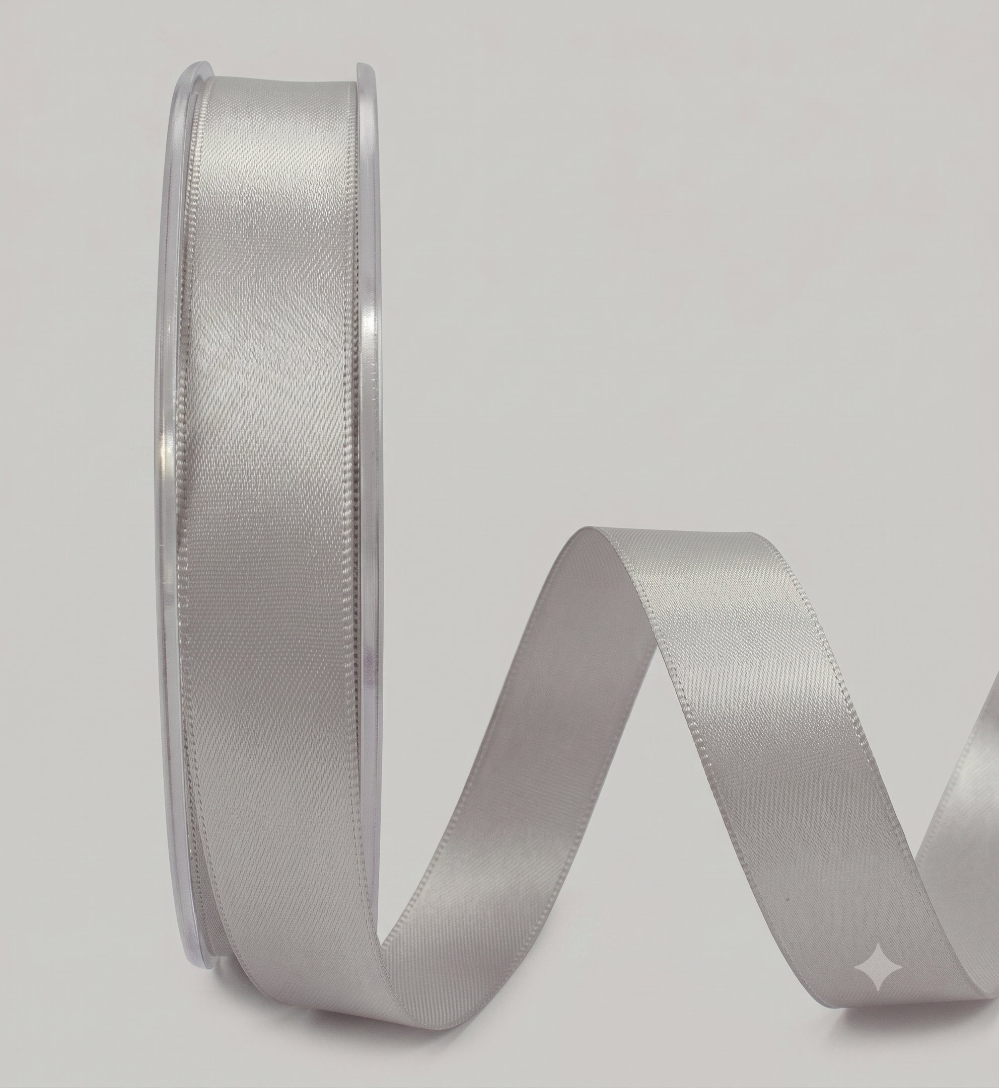 A spool of light silver satin ribbon with a single strand unwinding and curving to the right, set against a plain light gray background.