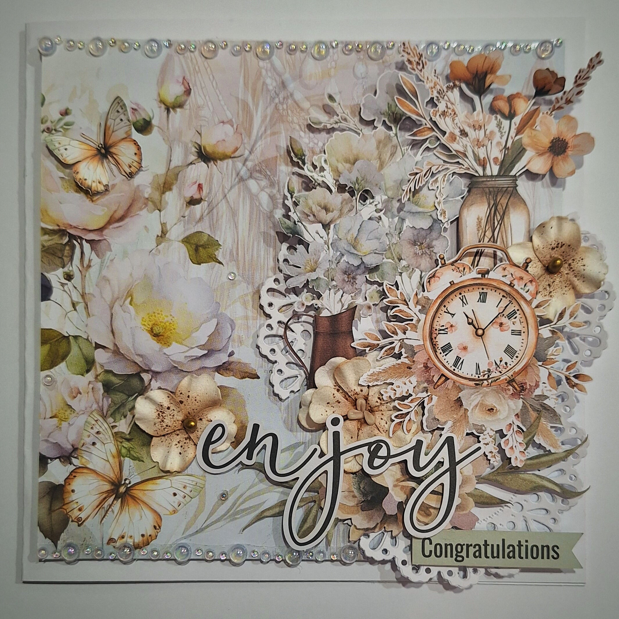 Decorative greeting card with flowers, butterflies, and a clock, featuring the word 'enjoy' and 'Congratulations'.