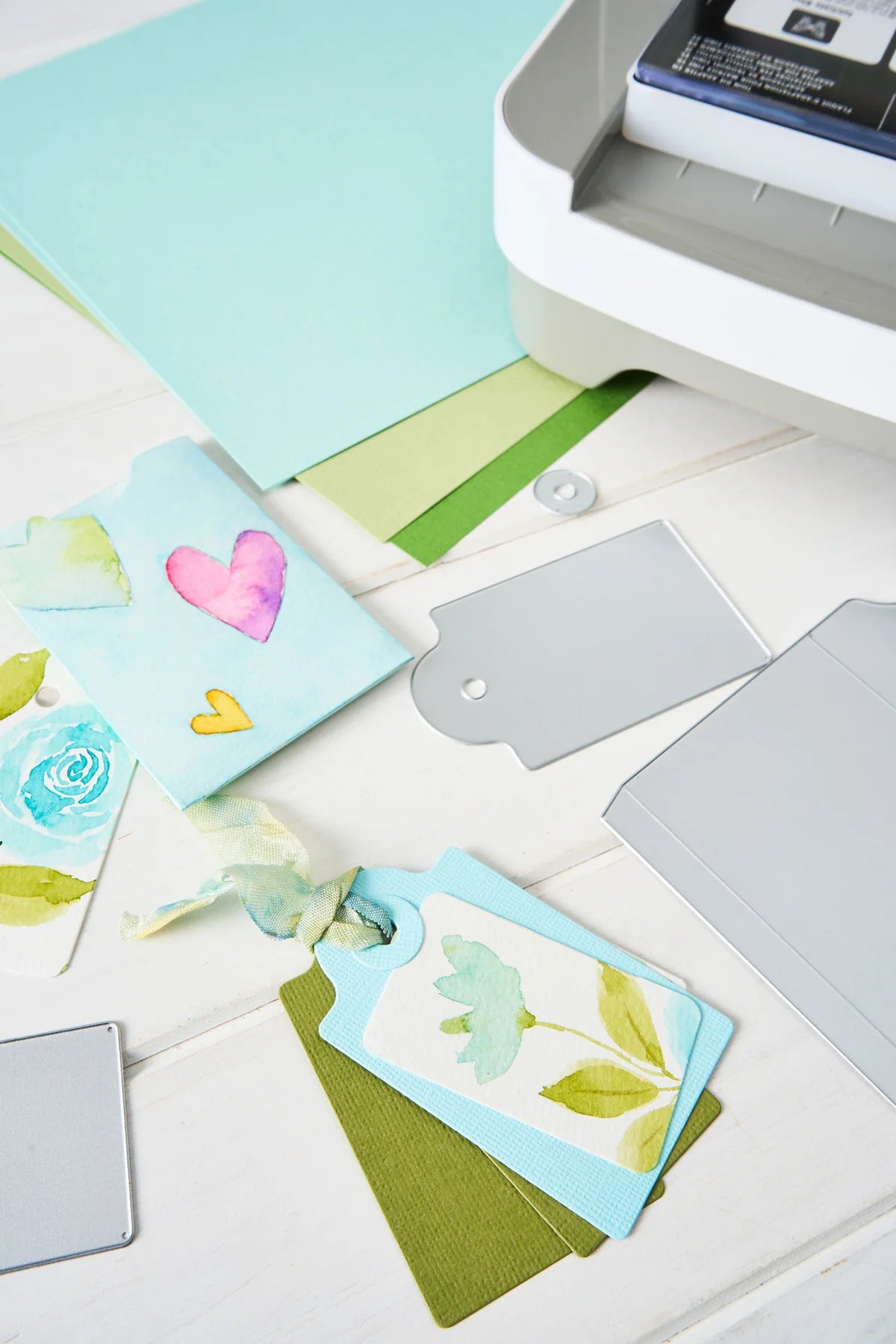 Colorful greeting cards with floral designs on a white surface next to a printer.