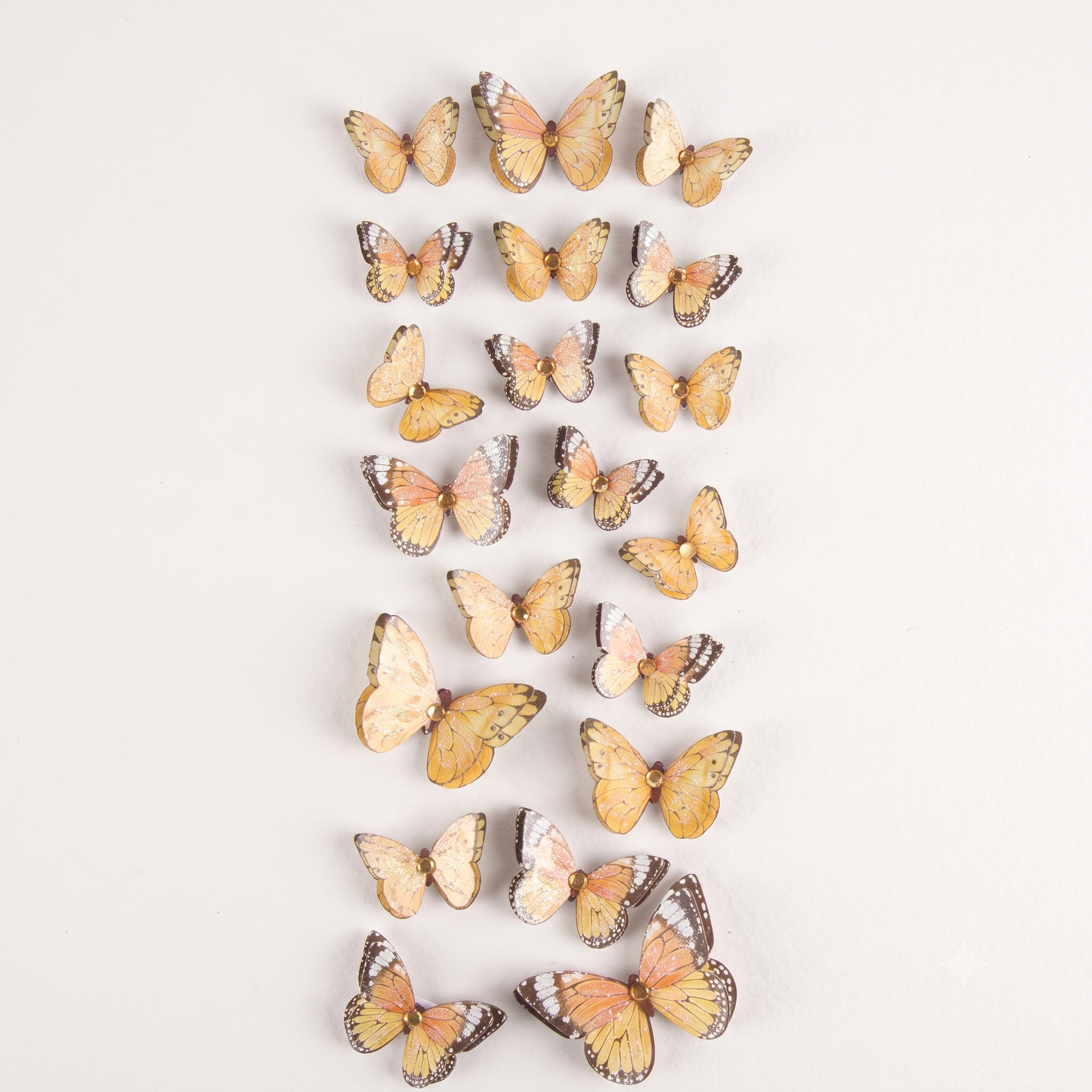 A vertical arrangement of multiple artificial butterfly decorations in shades of yellow, orange, pink, and brown on a plain white background.