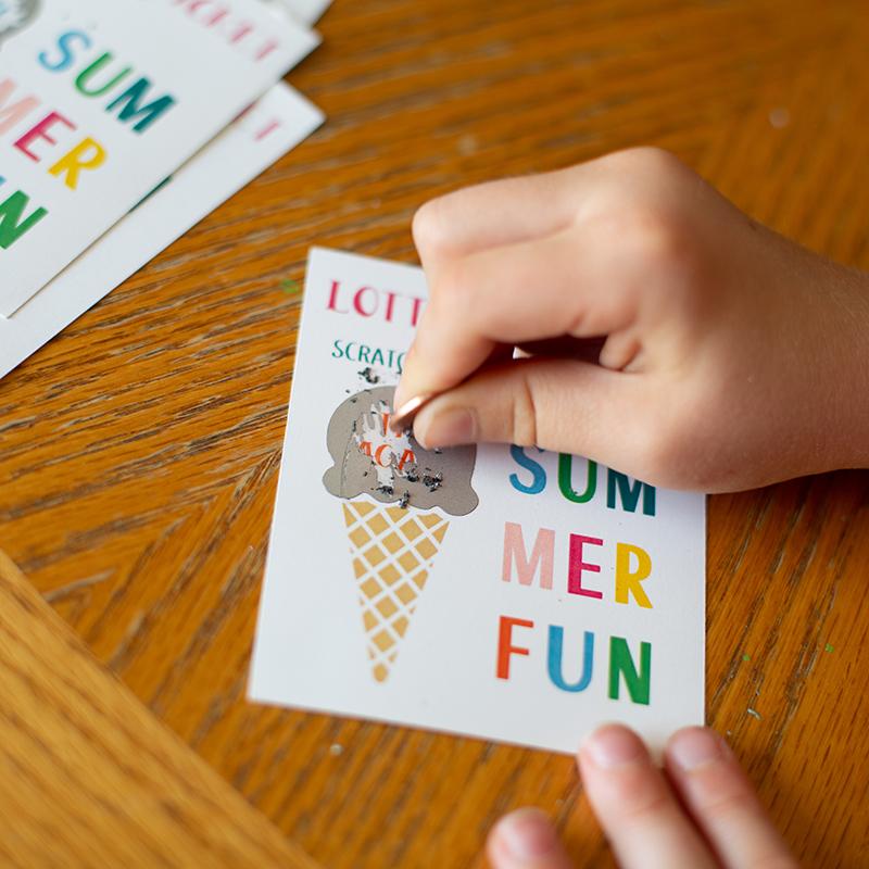 Hand scratching a silver sticker on a printed card to reveal the hidden message